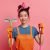 Cheerful housewife with cleaning tools on pink background.
