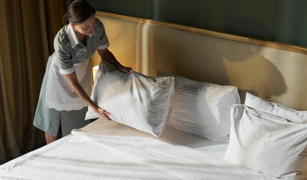 Housekeeper adjusting pillows and making bed in a modern hotel room. Neatly arranged white linens create a clean and welcoming atmosphere SSUCv3H4sIAAAAAAAACnxUPY/cIBDtI+U/rFwfCp82pEyRLlL6KMUA41t0XrMy9kVRdP892F47eLWXDt4w8x7DG/58/HA6VRZScNXn0595l/eh66Y0DjCG2GeYPt3wAXuPQ4m8DqKmJQCh3KEPYxwCdCVoYXTnHi6YwX7quhl+W4JVGmGcEqZCC3Rw+Z33Ymfw0WIao3sp0XSexhGHHS+KOhjxOas4lN2u/GPdn7bAEswZOVR9x3jtsLpRrDSTnSPfsK82dGV5p8QXhGn8/ekrpPPcy0elQnLYddBjnNK/ouvi537pZ+zd3Iad4/7G+0VySB6ION/LbvXu21gmM8rqhxl+QLikMSwPV2Y06sCn9aNsG54Xtus5jvGuwCH9y5RCjyk9FH0zQ5nslfUNByTOUEpk4w2x3AjikbXGeU0lMwcC0VonbUuJsA0nEpqWaONqgoIzbxtssKX/yNfFW+GnATuE1aQ3HRUK8M4JTkyDnsi61gQUKtIyDq52isl211Bxxig6SQlHjUQqOwu2lDgnWyfBcqfWDq4Xr15+5We+LOa9KYDJh1iY+TU66NKd7SFcYYBD3nUILvTPBRLH8zLQWyUXp34c5hbvj1J1MV7B5kH4fGozDW74GVLKx/2GlyOXv494KXj6OC4Nu1WtfJ7JecuEMLypheZUcWmM4VX5E5xDrrPI2QRO1y6CR38Yhc0WrJGaa6Zq/Y7P1wOSc/n03hytR2pl5O3l9x9mspeQT/6PmlOp/kutqCy0PaQ2jdioDz9jPhP8o5+xUpBNr7LlpZOOSN/WBFohiZeGaVTArN9/saOoiilaU2q0pPuBO1EVr0UeJ6a1WEx50xPmNlSohKZCG2KUZtn3uiG2AZfNz6mgIJuGu5z19hcAAP//AwDWlHiDZwYAAA==
